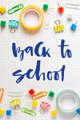 Back to school. Handwritten inscription. School supplies on white checkered paper