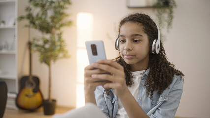 Obraz na płótnie Canvas Black teen in headphones chatting in social networks on phone, gadget addiction