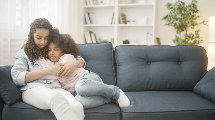 Obraz premium Caring african teen girl hugging and comforting sad little sister, family love