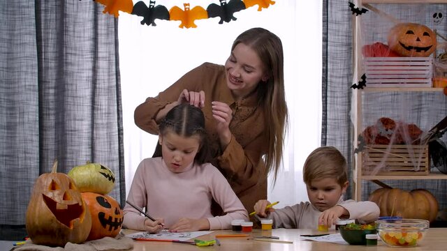 Happy family in a room decorated for Halloween. The boy plays with paints and pencils, the girl draws, and at this time her mother corrects her daughter's hair. Halloween. Slow motion. Close up.