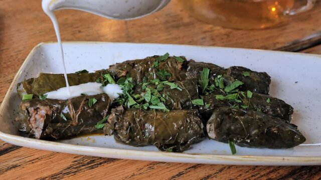 Plate of Delicious Stuffed Greek Wine Grape Leaves (dolmades) with with meat and rice, parsley and Poured oven White Sauce. Dolma. Sarma.