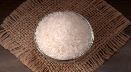 Bowl and spoon with sugar on wooden background.