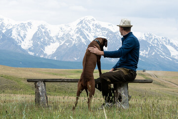 A guy with a dog sits on a bench and admires the mountain scenery. Traveling with a dog. Rhodesian...
