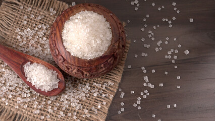 Bowl and spoon with sugar on wooden background.