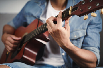 Enjoy handsome asian man practicing or playing the guitar on the sofa at living room