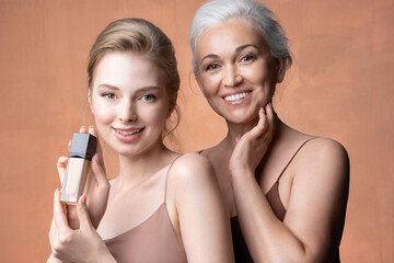 Beautiful female generations mature mother, young adult daughter with jar o foundation, makeup...