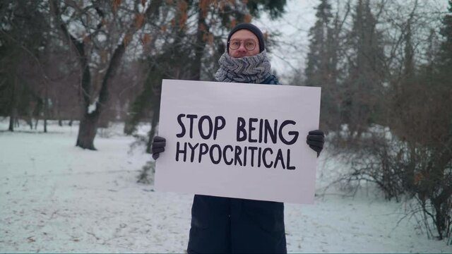 Man Standing in a Park. Holding a White Sign. Saying Stop Being Hypocritical. Taking Part in a Protest. Demanding Justice from the Government. People Are Irritated with Corrupt Institution and Policie