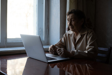 Happy senior woman sitting with her granddaughter looking at laptop making video call. Mature lady talking to webcam, doing online chat at home during self isolation. Family time during Corona