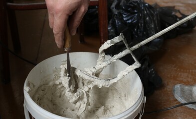 scraping with a small spatula the mortar from a construction mixer over a container, the hands of a...