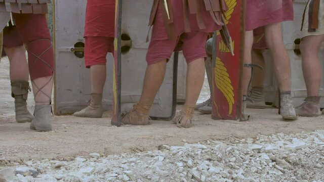 Legs close-up point Roman soldiers stand in leather shoes with shields and spears.