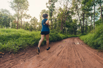 Fototapeta premium Trail running athlete through the in the rural road and tropical. Active woman trail runner running in the forest in the morning.