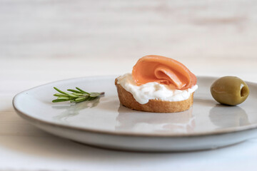 Salmon sandwich with fresh rosemary and pickled olives on gray plate over white background.