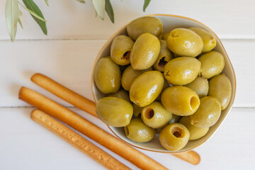 Pickled green olives on white wooden background.