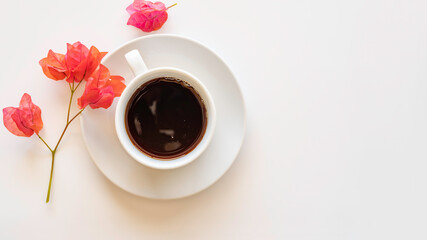 Coffee cup and sprig of Bougainvillia on white background with copy space.