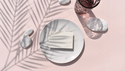 Summer tropical still life mockup composition. Blank invitation card, marble plate with sea pebbles on pink background. Harsh palm shadows, reflection.  Mock up for wedding invitation or business.