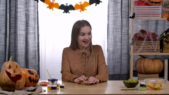 A young beautiful woman is sitting at a table in a room decorated for Halloween. Her daughter brought a small pumpkin with a terrible face, and her son a drawing. Slow motion. Close up.