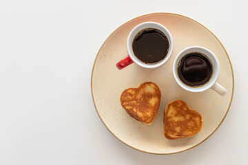 Coffee cups and heart shaped pancakes on beige plate over white background with copy space. Coffee break concept.
