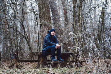 Man photographer sitting a the bench at the forest and preparing to taking picture of landscape in mountains. Man looking at the location with pleasure