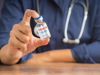 Hand of a doctor holding a COVID-19 vaccine bottle while sitting in the hospital or clinic. Vaccine for immunization, and treatment from coronavirus infection. Healthcare and medical concept