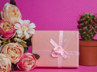 A photo of a bouquet of flowers, a gift in the form of a box and a cactus on a pink background, front view. High quality photo