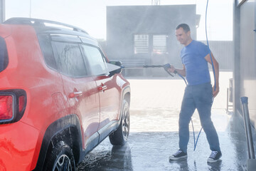 Car wash with high pressure water. Man washes the car outdoors, car wash