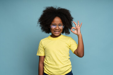 I'm okay. Portrait of adorable joyful little girl with curly hair in yellow T-shirt showing ok hand gesture and smiling, healthy happy contented with life. 