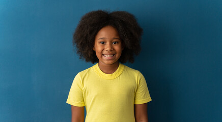 Portrait of cheerful little girl with curly hair in T-shirt smiling funny and carefree, showing front teeth. Healthy happy child, positive emotions concept. Indoor studio shot 