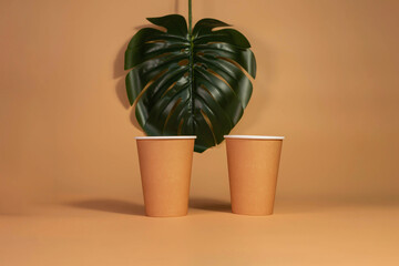 Monstera sheet, paper disposable eco-friendly cups on beige isolated background. Eco-concept.