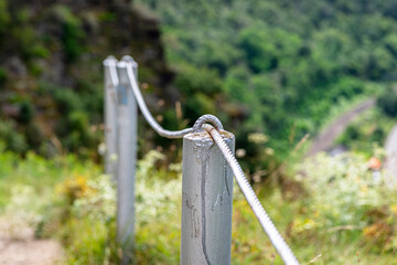 A steel rope passing through the meshes of metal posts over the cliff.