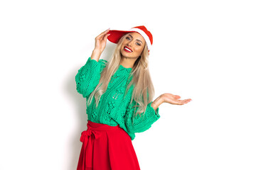 Portrait of beautiful woman in christmas santa cap, toothy smile, white background with copy space, studio shot, weared in green red color, holding hand