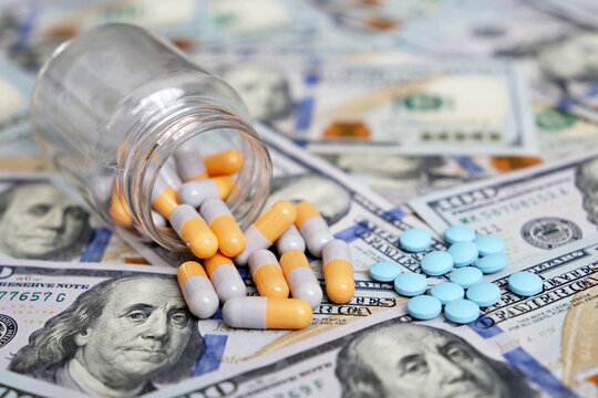 Pills and capsules on US dollar bills, medication scattered from the bottle. Concept of health care, pharmaceutical business, drug prices in USA, pharmacy