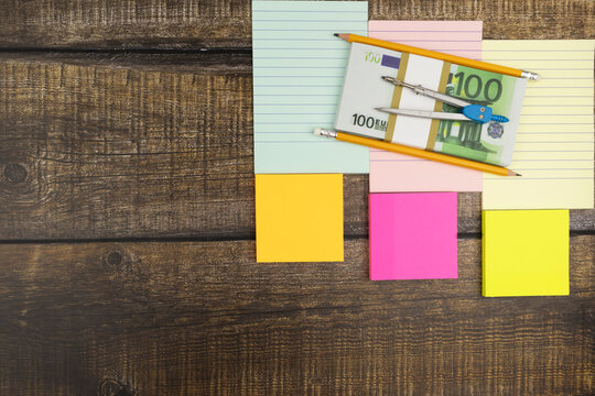 Business, financial or wealth concept with 100 Euro banknotes, a mathematical compass and sticky memos over a light wood background with copyspace placed to the corner. Flat lay, top view