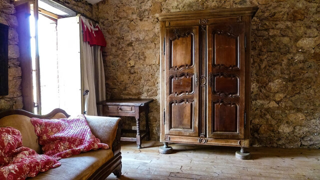 Grimod, France - June 9. 2016: View Into Room Of French Cottage Built Of Natural Materials In Style Prevencale With Natural Stone Wall, Antique Sofa And Wooden Wardrobe (focus On Wardrobe)