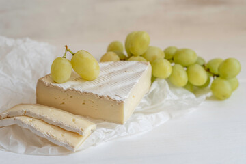 Brie cheese and white grapes on white wooden background with copy space.