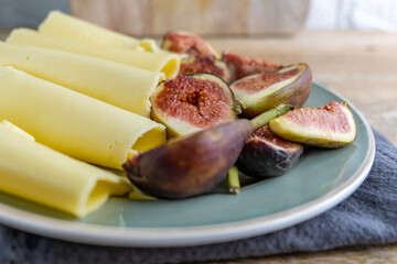 Sliced cheese and fig fruits on rustic plate over wooden background with copy space.