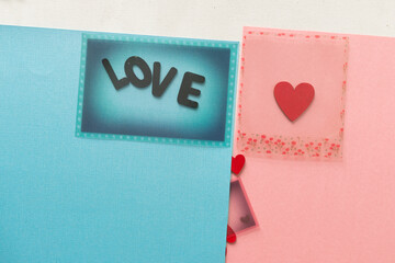 the word "love" in wooden letters on blue and pink construction paper background and a fancy plastic overlay - with red hearts