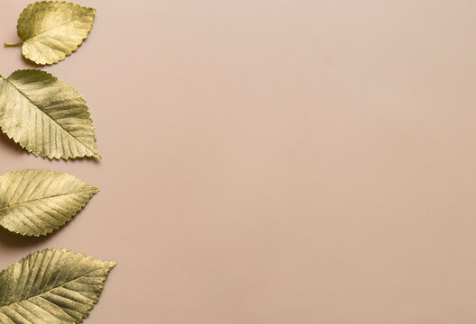 Leaves In Gold Paint On A Beige Background With A Horizontal Stripe On The Left. Autumn Concept. Top View Of Autumn Leaves In Gold Paint On Beige With Copy Space For Your Text To The Right.