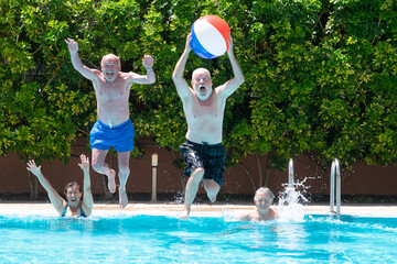 Happy group of mature people enjoying summer and swimming pool, jumping and playing with inflatable ball