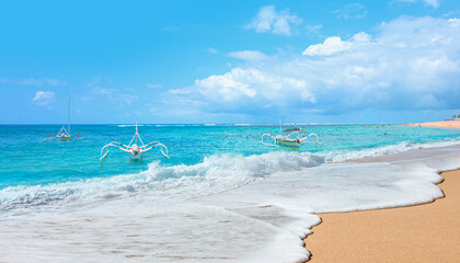 Tropical sandy beach and clear sea background with traditional balinese boats - Tourists walking and sunbathing on the beach in the morning - Bali, Indonesia 