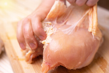 Chef's hands peeling raw chicken breast. Close up