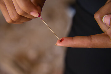 detail of a needle sticking in the finger of a seer woman who does voodoo.