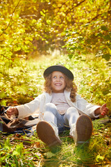 Portrait of young funny girl with blonde curly hair and in black hat in an autumn park on a yellow and orange leaf background