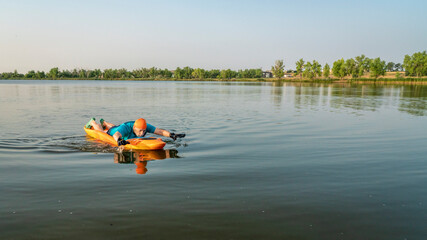 athletic, senior man is paddling a prone kayak on a lake in Colorado, this water sport combines aspects of kayaking and swimming