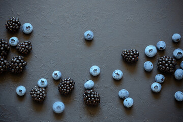 Freshly picked blueberries and blackberries, scattered on a black textured desk surface. Flat lay.