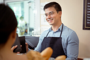 Obraz premium Smiling barista giving online payment to customer , pay for the order in a cafe shop