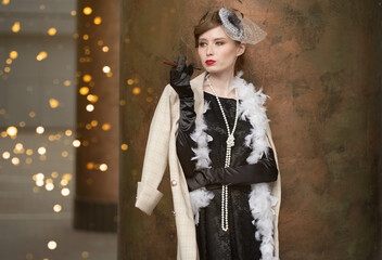 A young beautiful woman in a historical costume of the 20s or 30s of the XX century with a boa and...