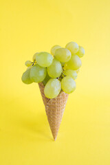 Ice cream cone with green grapes on the yellow background. Location vertical.