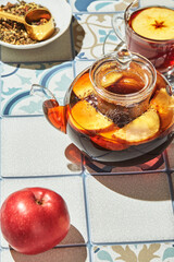 Fruit tea with apples and thyme in glass teapot and cup on table made of colored tiles