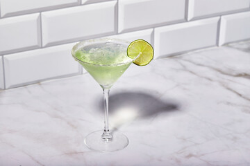Martini cocktail with ice and slice of lime on marble table background. Alcoholic cocktail or non-alcoholic mocktail.