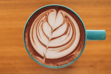 Close up of blue cup of coffee with full latte art on wooden table.